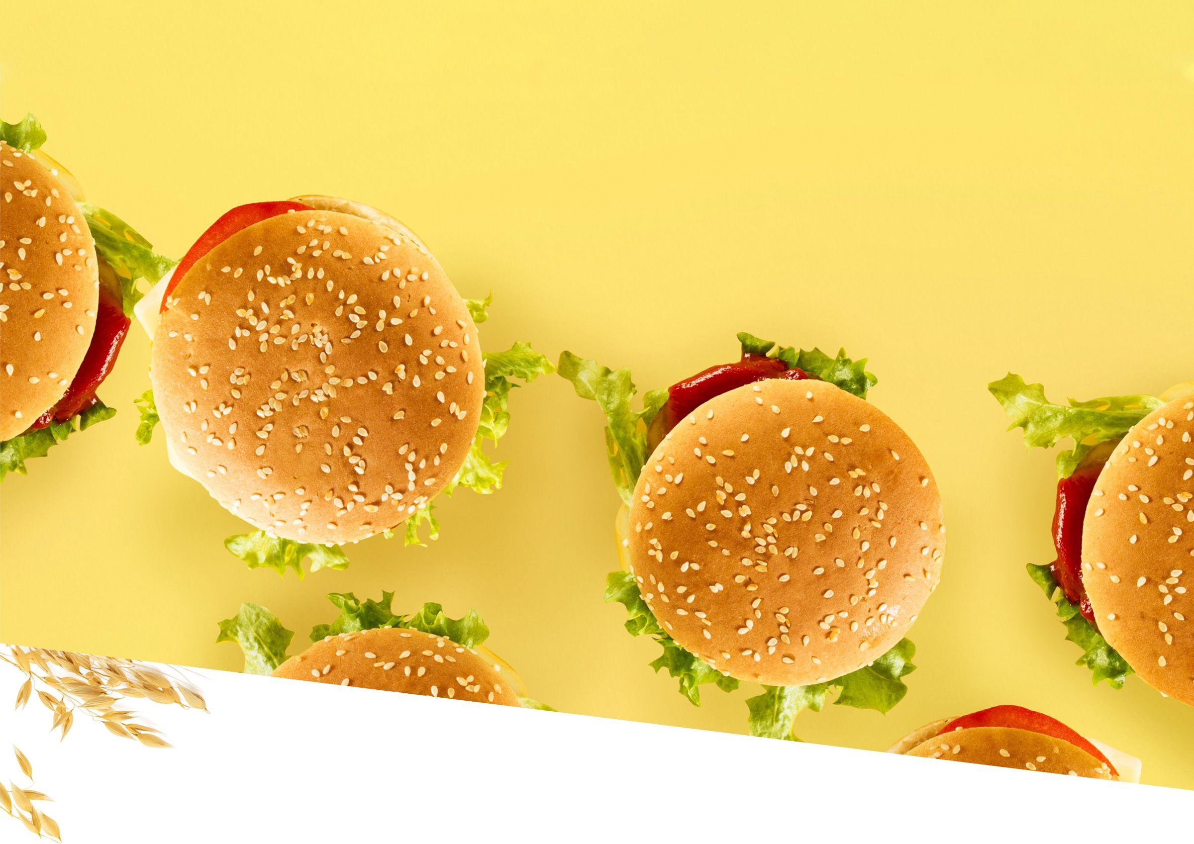 Burgers with sesame seed buns on yellow surface.